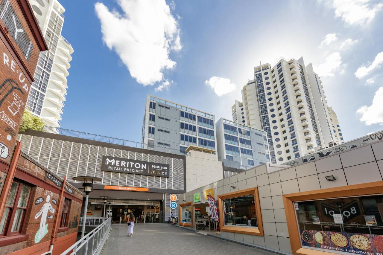 Meriton Suites Bondi Junction Sidney Exterior foto The photo depicts a modern urban environment featuring a building labeled "Meriton Retail Precinct." In the foreground, there are shops with colorful signage, while in the background, tall residential buildings tower over the area. The sky above is b