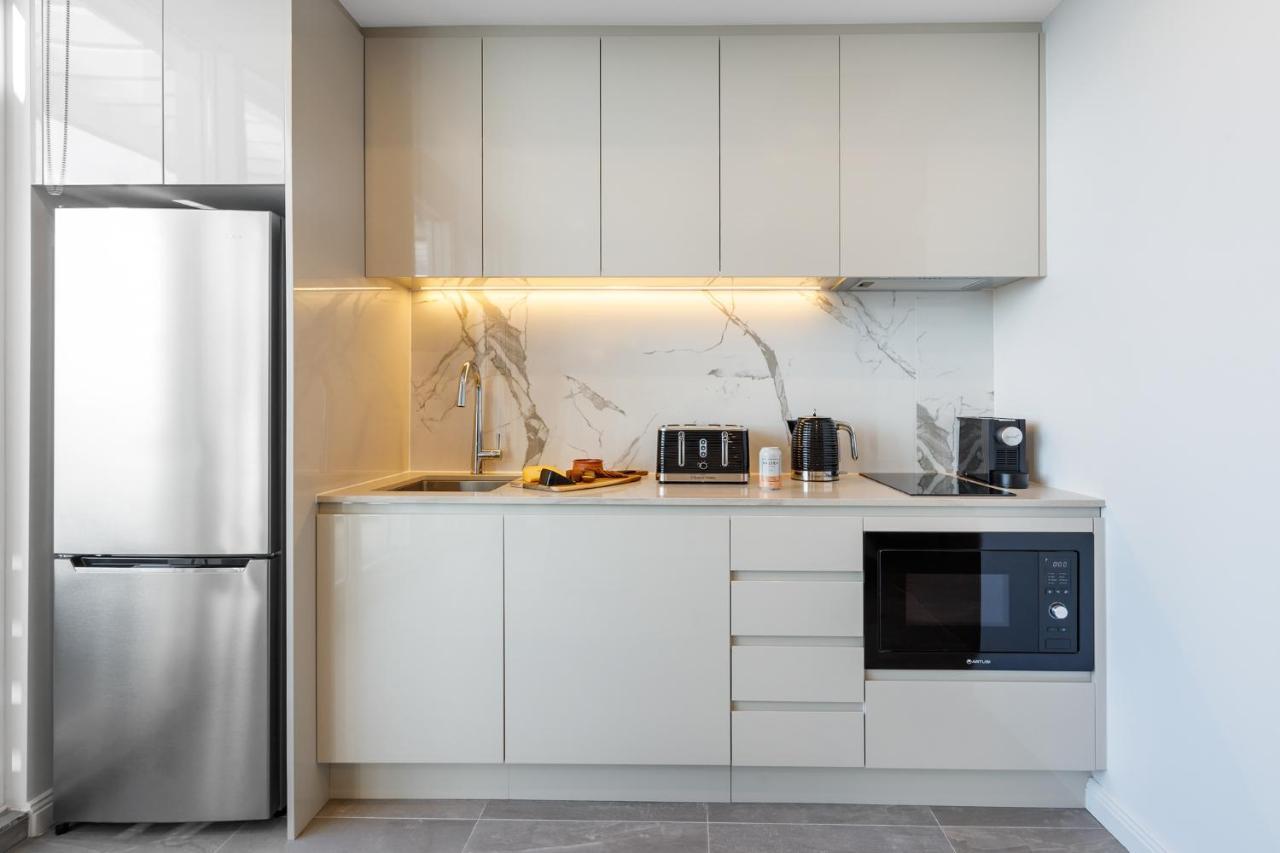 Meriton Suites Bondi Junction Sidney Exterior foto The photo shows a modern kitchen featuring a sleek design. It includes light-colored cabinetry with a smooth finish and upper cabinets that blend seamlessly with the wall. The countertop is made of a light stone, complementing the overall aesthetic. 