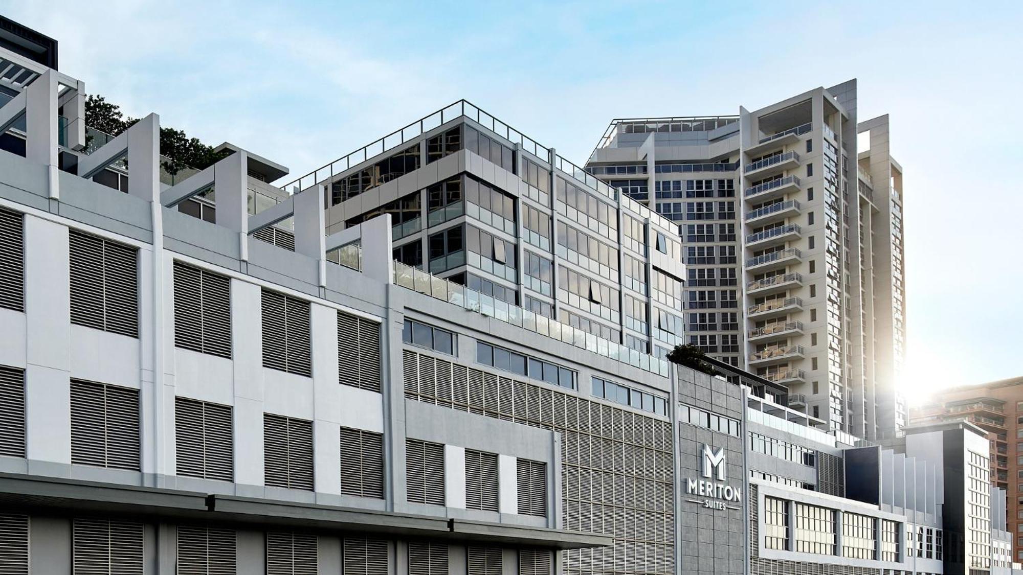 Meriton Suites Bondi Junction Sidney Exterior foto The image shows a modern urban building or complex. The structure features a combination of glass and concrete elements, showcasing contemporary architectural design. The foreground has a lower section that appears to be a podium or base with a textu