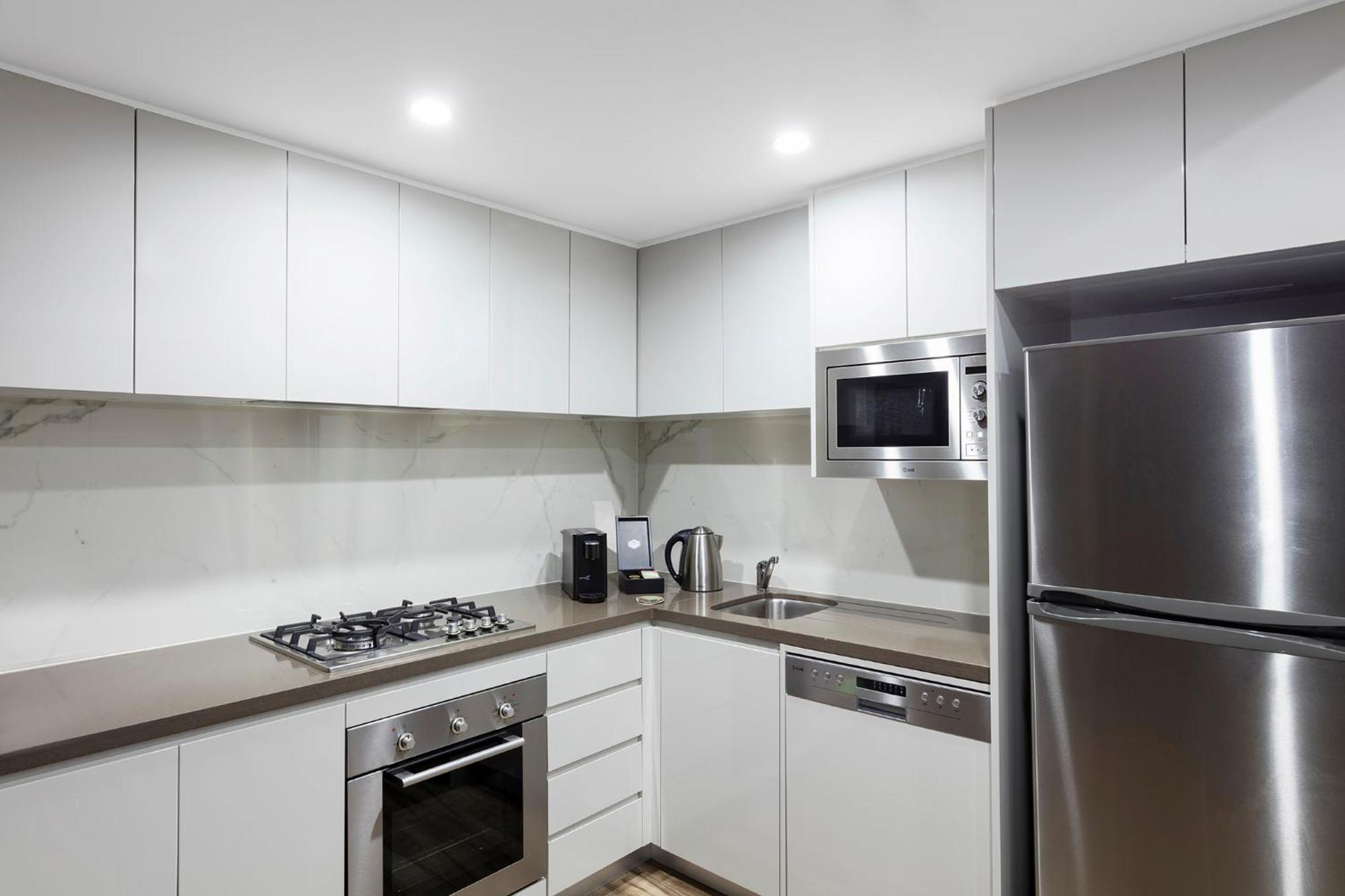 Meriton Suites Bondi Junction Sidney Exterior foto The photo shows a modern kitchen featuring a minimalist design. It has light-colored cabinetry, a countertop, and stainless steel appliances. The appliances include a gas stove with multiple burners, an oven, a microwave, a kettle, and a refrigerator